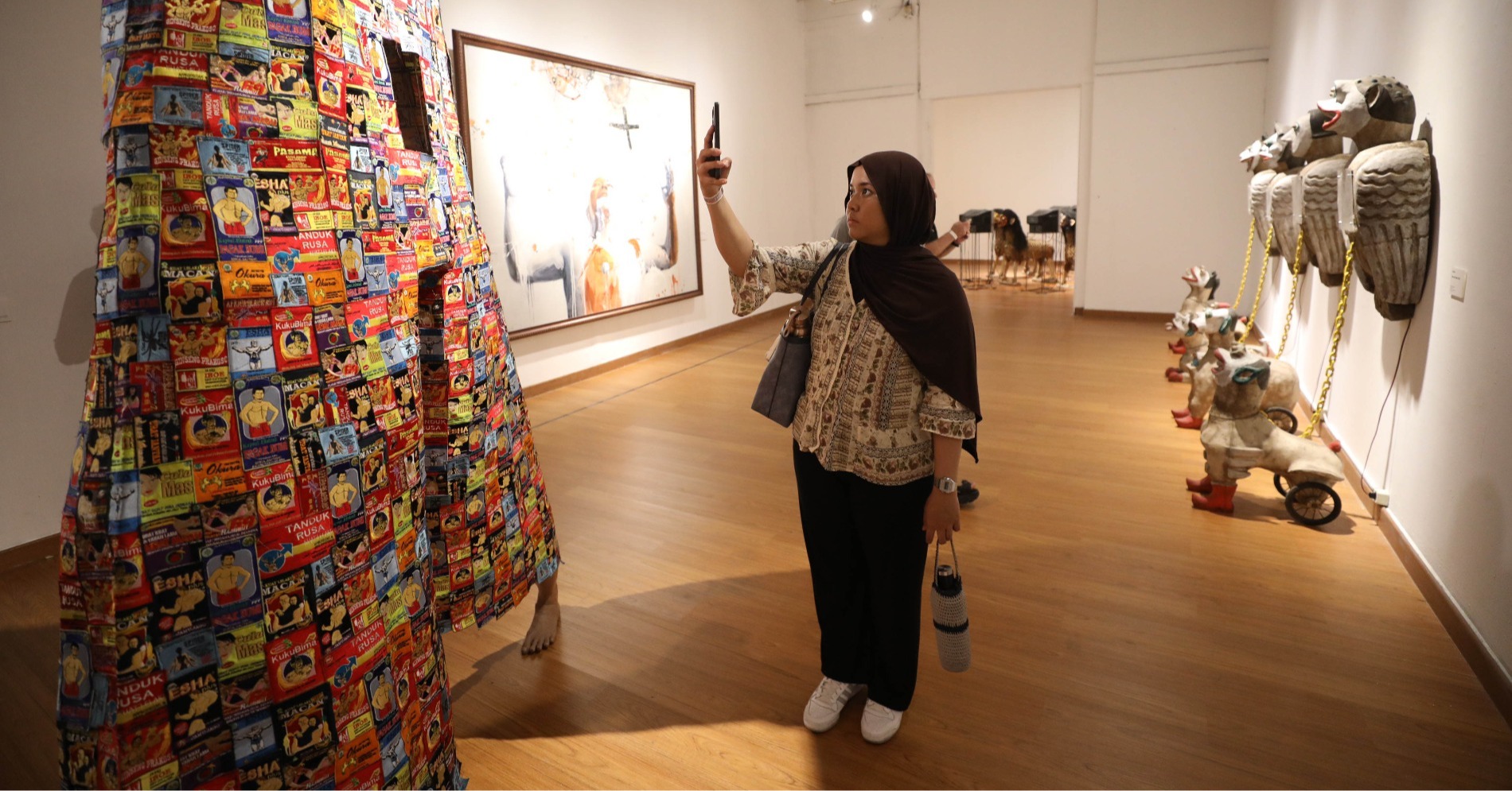 Seorang pengunjung memotret karya Mella Jaarsma dalam pameran Flaneur: Kembara Lintas Dunia di Gedung A, Galeri Nasional Indonesia pada Kamis (17/10/24) (Sumber gambar: Hypeabis.id/Eusebio Chrysnamurti)