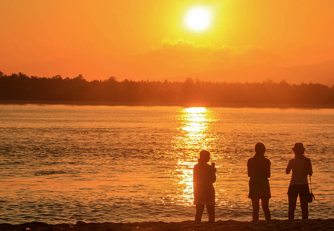 Wisatawan menikmati suasana matahari terbit di Gili Trawangan, Lombok, Nusa Tenggara Barat. Pulau seluas 340 ha ini merupakan pulau terbesar sekaligus pulau teramai dibanding dua pulau lainnya, yakni Gili Meno dan Gili Air. Pasir putih serta laut biru menjadi andalan bagi ketiga pulau yang terletak di utara Pulau Lombok ini. Beragam aktivitas bisa dilakukan di Gili Trawangan, mulai dari berjemur, snorkeling dan diving.