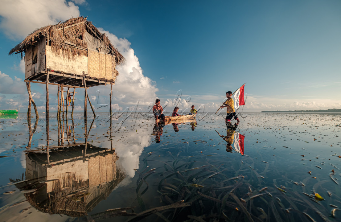 Di pagi yang cerah itu anak-anak suku Bajo Sampela, di Desa Samabahari, Kecamatan Kaledupa, Kabupaten Wakatobi, Sulawesi Tenggara yang bermukim di tengah laut (terpisah dari daratan), bermain di air laut yang sedang surut. Saat merekea sedang bersantai di atas perahu di tengah hamparan lamun, ada anak yang datang bergabung sambil membawa bendera merah putih di pundaknya.<br />
<br />
Di pagi itu, bendera merah putih terlihat begitu indah di kampung Bajo, di hadapan anak-anak suku Bajo.<br />
&nbsp;