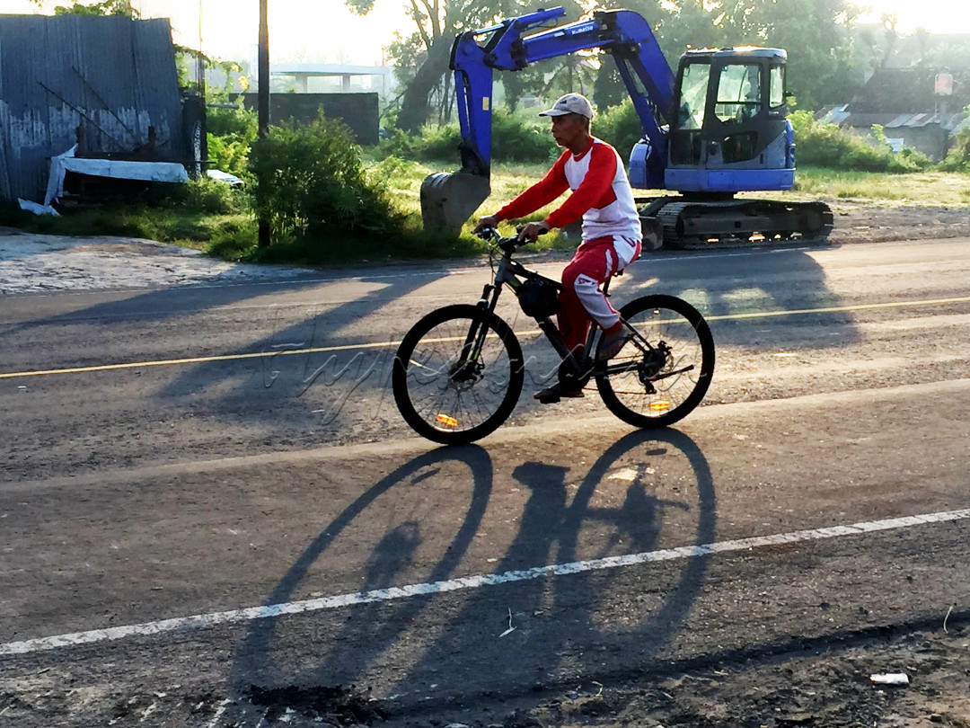 Se orang bapak bersepeda pagi hari dan mengenakan pakaian Merah Putih, sebagai rasa nasionalisme yang tinggi.