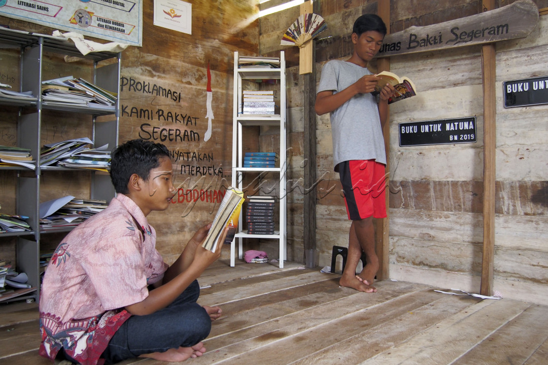 Dua orang pemuda sedang membaca buku yang mana didinding tertulis "Proklamasi Kami Rakyat Segaram Menyatakan Merdeka dari Kebodohan" di perpustakaan desa Segaram&nbsp; di Kabupaten Natuna, 25 September 2020.