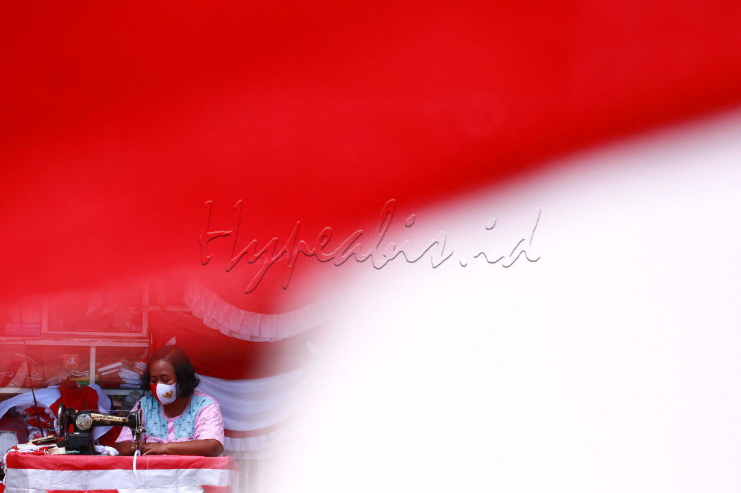 Sejinah (55) menjahit kain bendera merah putih di Kampung Bendera Darmo Kali, Surabaya. Menjelang perayaan HUT ke-76 RI, sejumlah pedagang bendera musiman mulai terlihat menggelar lapaknya di kawasan ini. Dagangan yang dijajakan mulai dari pernak-pernik bernuansa merah putih.<br />
<br />
Sebagai pedagang pernak-pernik menyambut HUT RI, berjualan pada masa pandemi dirasa berat olehnya. Sejinah sudah 15 tahun berjualan, hampir setiap tahun menggelar dagangan bendera dan pernak - pernik bernuansa merah putih mulai dari harga paling murah Rp. 5.000 hingga ratusan ribu per buah tergantung jenis dan ukurannya.<br />
<br />
Tahun ini penjualan mengalami peningkatan penjualan, dibandingkan tahun lalu tidak ada kegiatan untuk menyemarakkan Hari Ulang Tahun Republik Indonesia. Meski demikian, dirinya tetap mencoba peruntungan rezeki momentum peringatan kemerdekaan RI yang masih diserang pandemi walaupun omsetnya menurun.