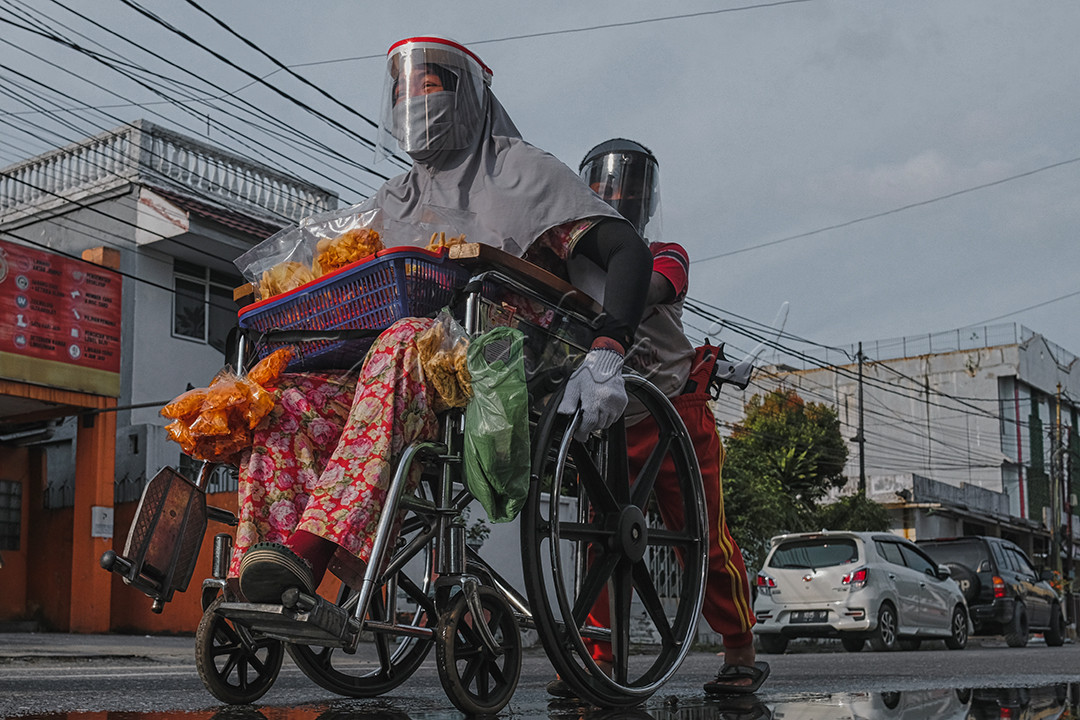Seorang anak membantu mendorong kursi roda ibunya saat berjualan makanan keliling di ruas jalan durian,Kota Pekanbaru, Riau. Berjuang untuk ekonomi di tengah pandemi, mereka menggunakan pelindung wajah dan masker untuk melindungi diri&nbsp; dan pembeli dari penyebaran Covid-19.