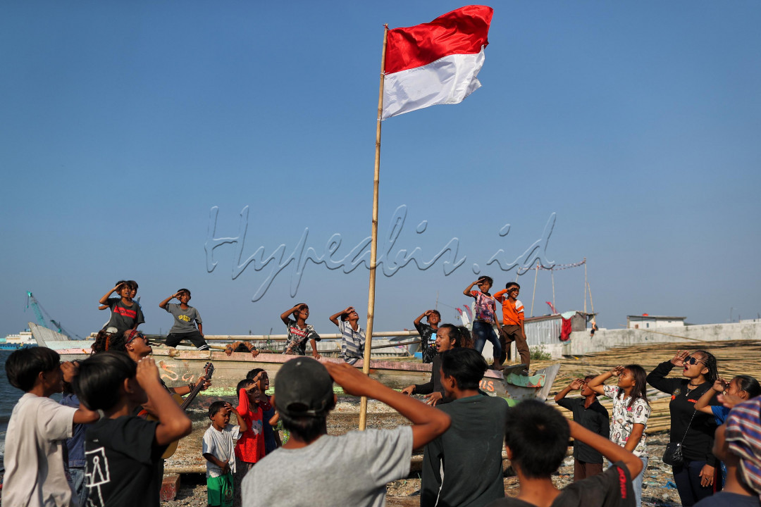 Anak-anak di perkampungan nelayan, Kali Baru, Cilincing, Jakarta Utara, memberi hormat saat mengikuti upacara penurunan bendera HUT ke-76 RI yang diadakan seniman jalanan di tepi pantai Kali Baru, Selasa (17/8/2021). Mereka mengikuti upacara dengan antusias.
