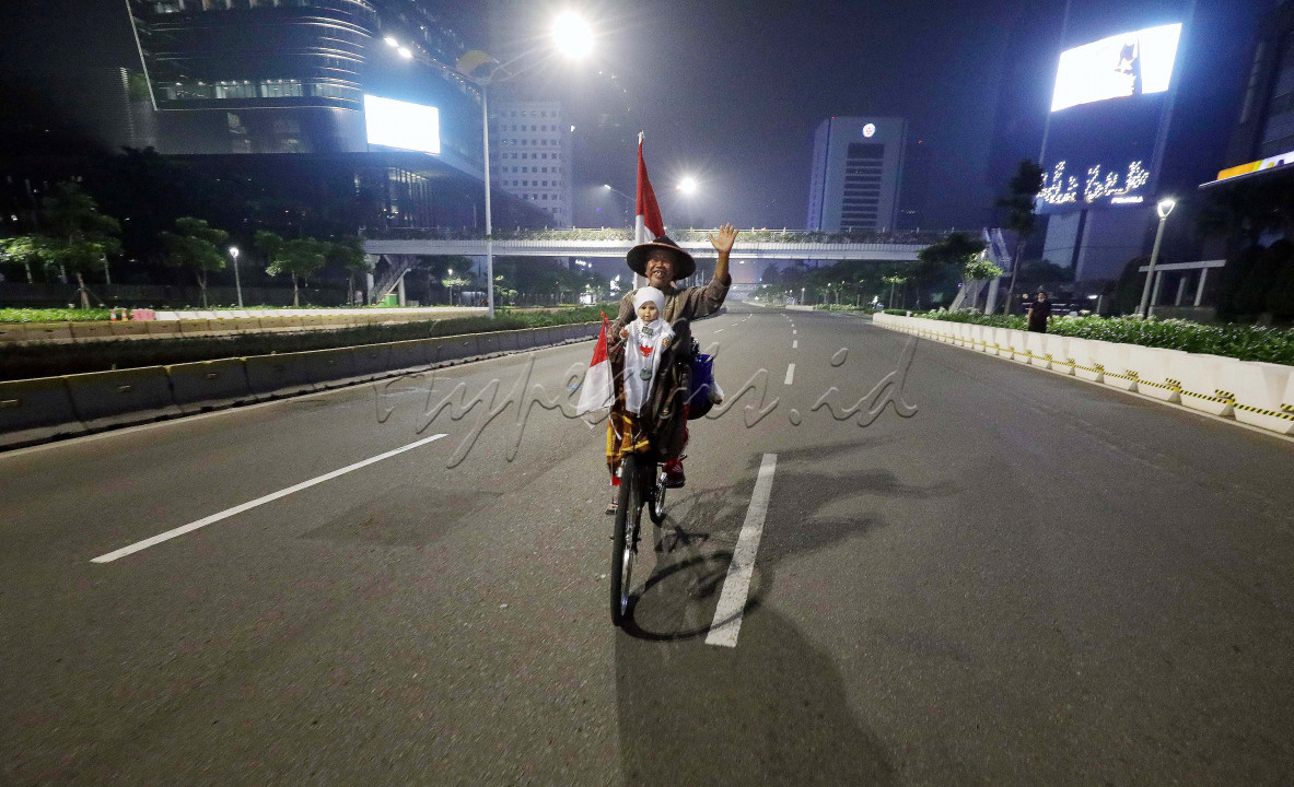 Pesepeda dengan atribut bendera merah putih melewati jalan yang terlihat sepi di kawasan Sudirman, Jakarta, Rabu (12/5/2021) malam. Sang pesepeda mengekspresikan jalanan lengang dengan menggunakan sepeda beratribut merah putih