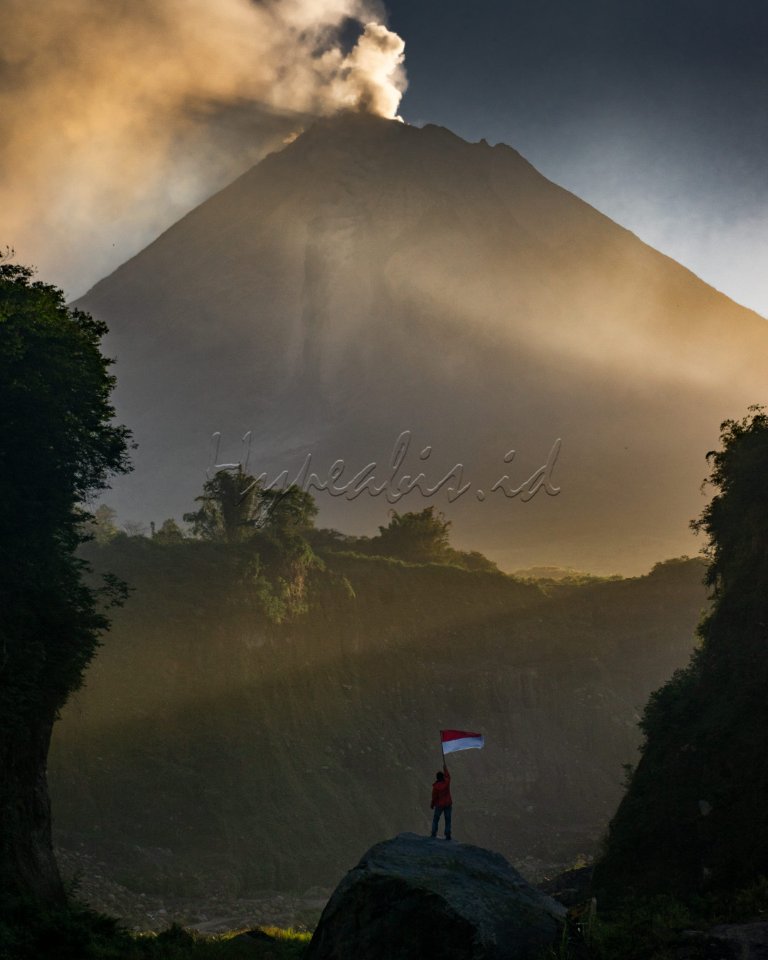 Seorang laki-laki yang berdiri disebuah batu besar dengan mengibarkan sang merah putih dengan latar belakang gunung merapi yag sedang erupsi. saat ini Indonesia sedang dalam kondisi tidak baik-baik saja, ditandai banyak bencana alam dan diperparah dengan adanya penyebaran virus corona. besar harapan saya untuk bisa berdamai dengan alam.