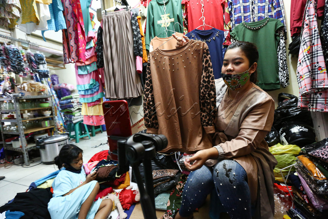 Vera, pedagang pakaian di Pasar Gondangdia, Jakarta Pusat menawarkan pakaian melalui siaran langsung di media sosial, Senin (28/12/2020). Vera sepinya pengunjung pasar tempat ia berdagang karena pembatasan yang dilakukan pemerintah berdampak pada usahanya. Untuk menyiasati kondisi tersebut ia menjual pakaiannya secara daring melalui media sosial di masa pandemi Covid-19 ini. Pakaian yang dijual seharga Rp. 35.000 per potong ini diminati pembeli secara daring. Pedagang mengakui mampu menjual 8 hingga 10 lusin pakaian per hari.<br />
<br />
&nbsp;