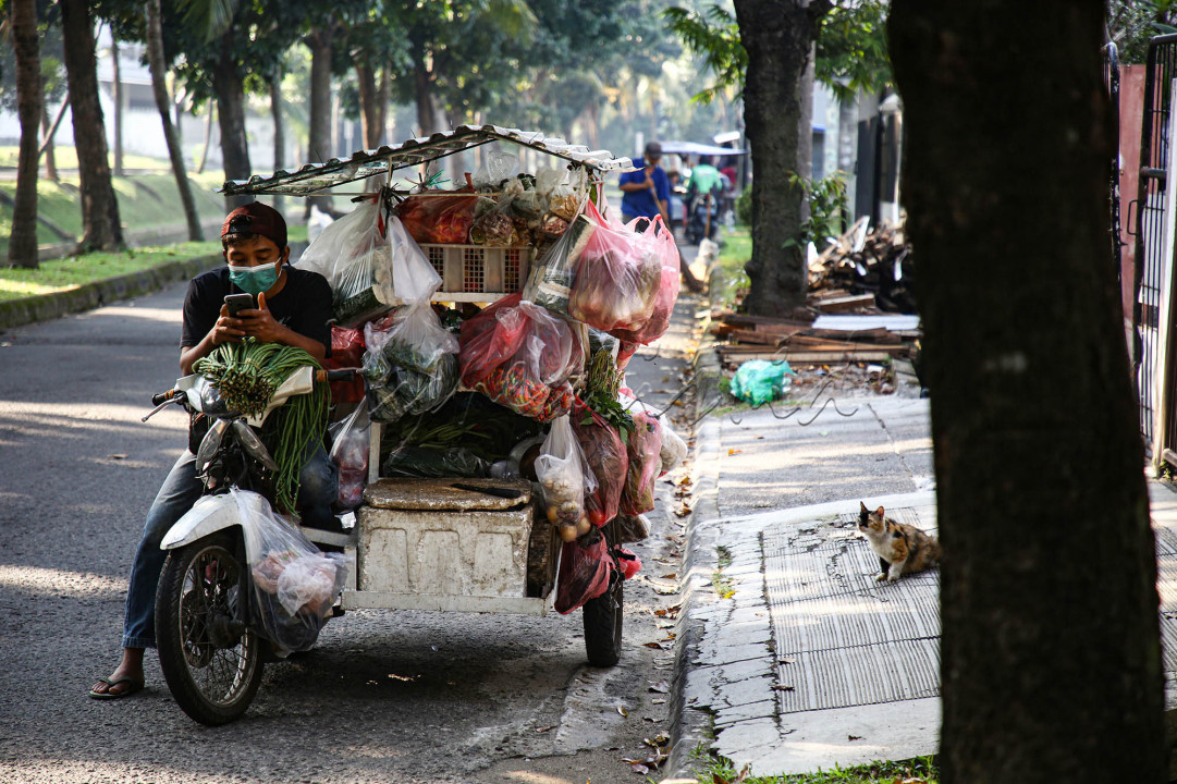 Bejo, pedagang sayur keliling memeriksa telepon selulernya terkait pesanan sayur dari para pelanggannya di &nbsp;kawasan perumahan Bintaro, Tangerang Selatan, Banten, Kamis (5/8/2021). Di masa pembatasan karena pandemi Covid-19, yang membatasi aksesnya ke sejumlah kluster perumahan disiasati Bejo melalui layanan pesan antar secara daring melalui whatsapp.&nbsp;<br />
&nbsp;