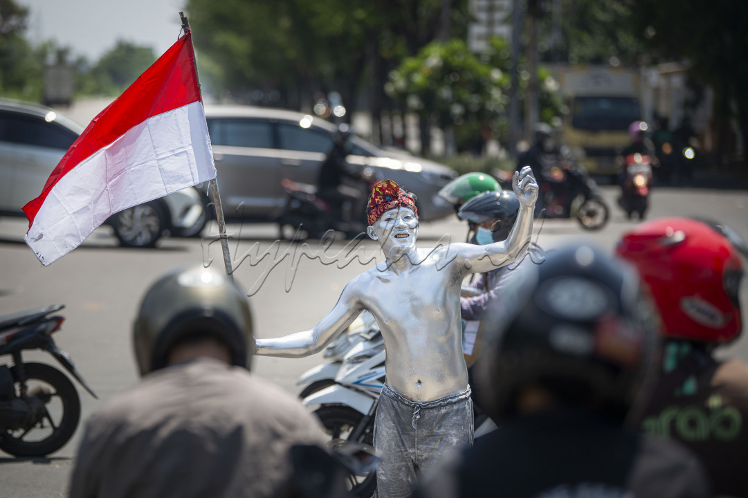 Pengamen 'manusia silver' membawa bendera merah putih saat beraksi di salah satu persimpangan jalan di Sunter, Jakarta, Kamis (12/8/2021). Sejumlah pengamen 'manusia silver' setempat juga menggunakan pernak-pernik merah putih, seperti bendera dan ikat kepala untuk memeriahkan hari ulang tahun (HUT) ke-76 Republik Indonesia.&nbsp;