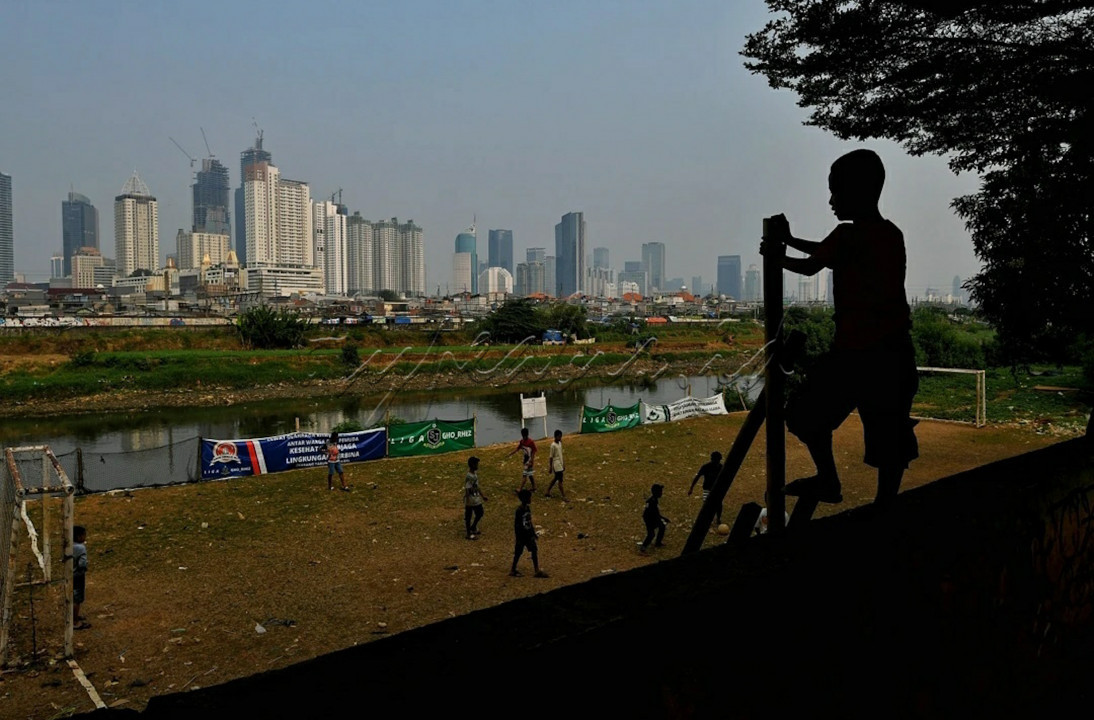 Anak-anak bermain sepakbola di bantaran kali Ciliwung, Jakarta, dengan latar belakang gedung bertingkat.&nbsp;