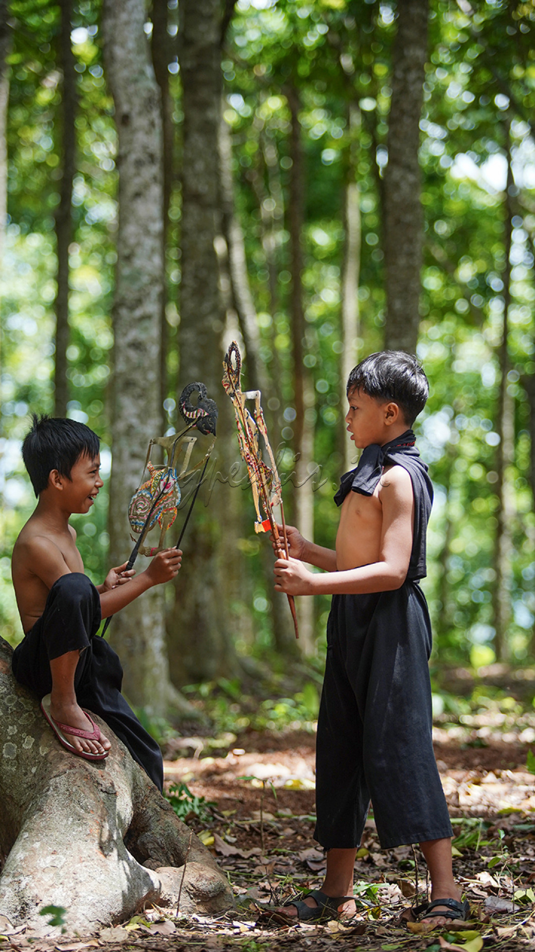 Dua anak sedang bermain dengan Wayang Kulit sebagai warisan budaya leluhur. Rasa bangga akan warisan budaya ini harus ditanamkan sejak dini kepada generasi muda terutama anak-anak.