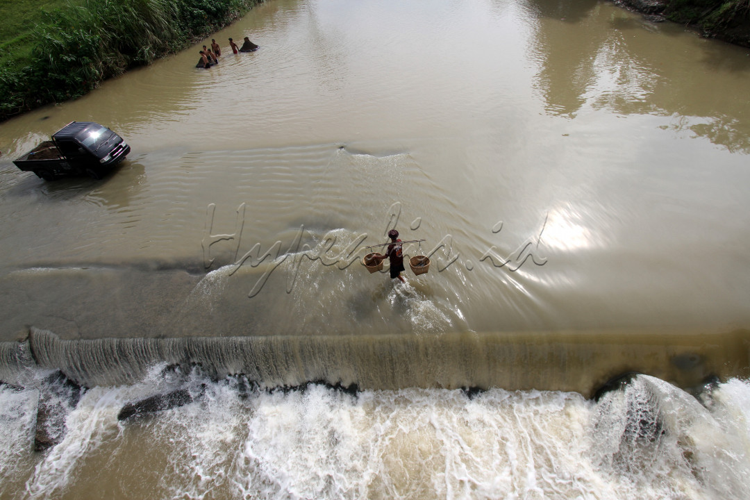 Warga menerobos jalan alternatif yang tergenang luapan sungai Cileungsi di Kabupaten Bogor, Jawa Barat.