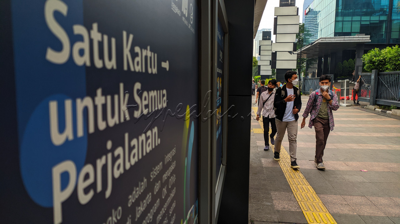 Warga melintas di samping iklan layanan masyarakat kawasan Bundaran HI, Jakarta, Sabtu (28/5/2022). Alat transaksi nirsentuh yaitu kartu JakLingko mempermudahkan masyarakat untuk menikmati antarmoda transportasi dengan tarif dan rute yang terintegrasi dengan satu kali tap dan satu tarif.