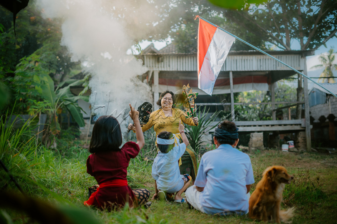 Sudah hampir 77 tahun lamanya, proklamasi pertama kali di kumandangkan oleh Bapak Ir. Soekarno. Dengan demikian title sebagai &lsquo;Negara Merdeka&rsquo; mulai disandingkan kepada Negara tercinta ini. Akan tetapi MERDEKA bukan berarti BEBAS sepenuhnya, melainkan banyak tantangan yang harus di lalui oleh bangsa ini, terlebih &nbsp;lagi Negara Indonesia merupakan bangsa yang sangat beragam. Keberagaman bangsa ini selain menjadi tantangan, juga menjadi sebuah anugerah tersendiri yang dimiliki oleh Bangsa ini. Bagaimana tidak, keberagaman yang dimiliki Indonesia mampu menempatkan Bangsa ini menjadi salah satu destinasi wisata dunia.&nbsp;<br />
&nbsp;<br />
Dengan demikian, keberagaman yang dimiliki oleh bangsa ini harus senantiasa dilestarikan dan dikembangkan kepada generasi penerus bangsa. Sehingga keberagaman yang dimiliki oleh bangsa ini dapat senantiasa bertahan di era gempuran teknogi saat ini.<br />
<br />
Selayaknya pada foto ini, seorang nenek memperkenalkan salah satu kebudayaan Indonesia melalui cerita-cerita lucu yang dipadukan dengan tokoh-tokoh pewayangan. Di mana kebebasan untuk mengutarakan pendapat sangat terbuka luas pada foto ini, sehingga tidak membunuh rasa ingin tahu anak kepada kebudayaan daerahnya di tengah perayaan kemerdekaan Indonesia.<br />
<br />
Nama : Kadek Gopala Sai Wiswadara Arista&nbsp;<br />
Tanggal pengambilan foto : 6 Agustus 2022<br />
Lokasi : Tumbu, Karangasem-Bali