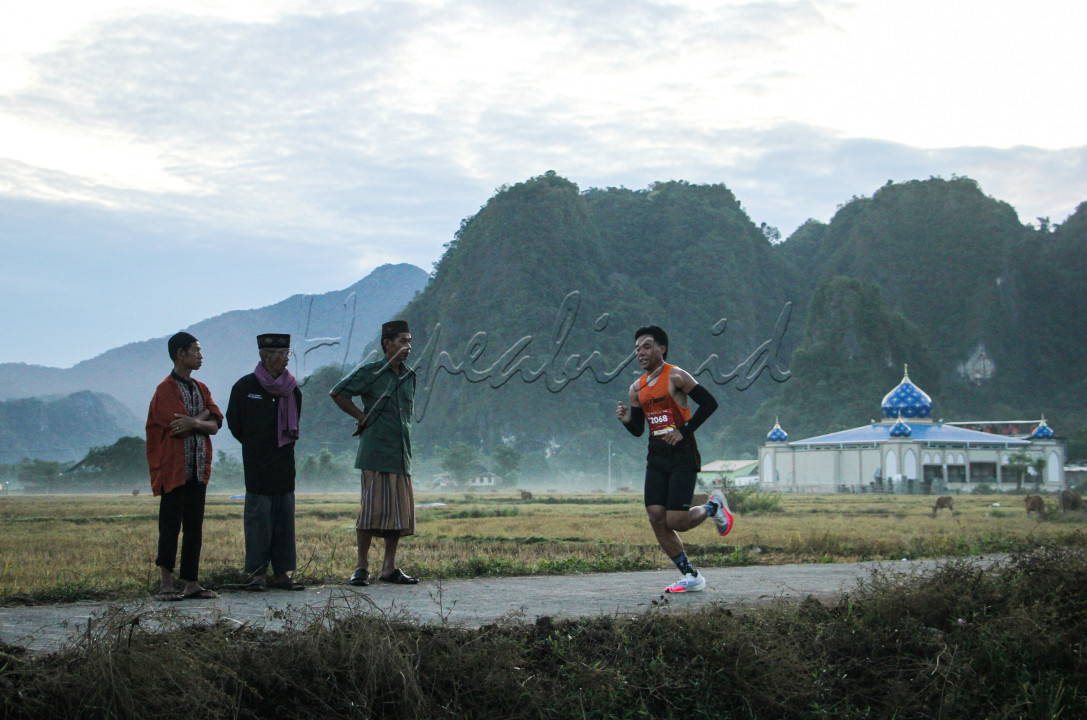 Warga menonton peserta yang mengikuti lomba lari Geopark Half Marathon 2023 dengan latar belakang gunung karst di kawasan Geopark Maros Pangkep di Kabupaten Maros, Sulawesi Selatan, Minggu (25/6/2023).
