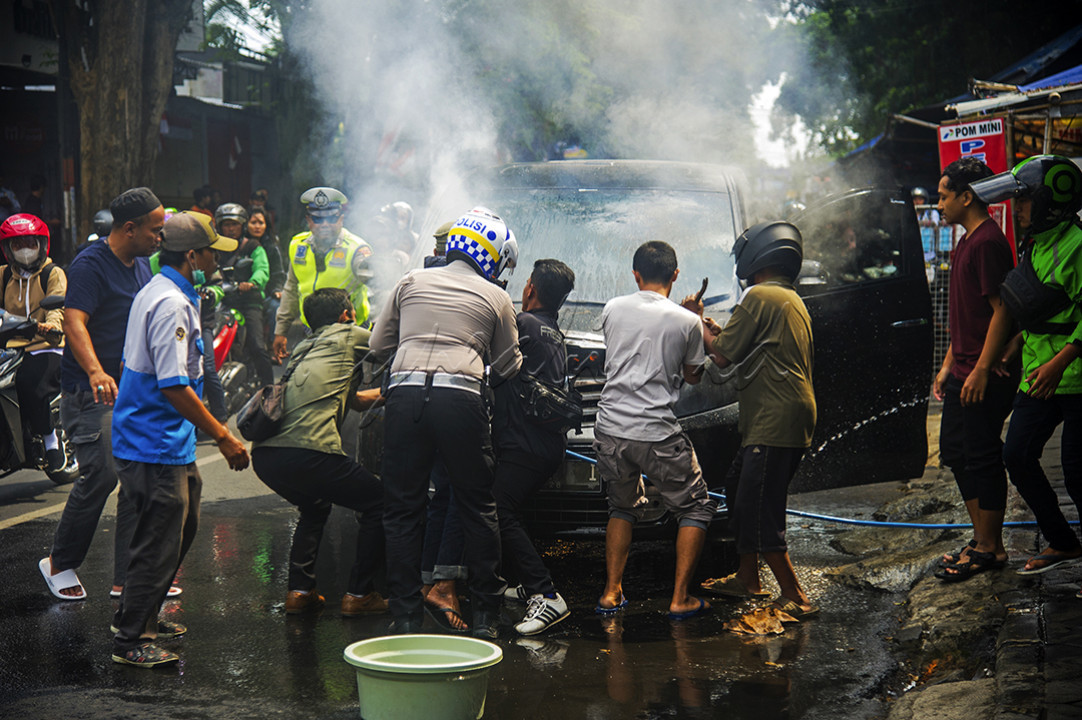 Aksi anggota Polisi Lalu Lintas (polantas) Polres Jember dan warga bahu membahu padamkan sebuah mobil yang terbakar di Jalan Jawa, tepatnya kawasan kampus Universitas Jember, Kecamatan Sumbersari, Jember, Jawa Timur (30/07/2023).