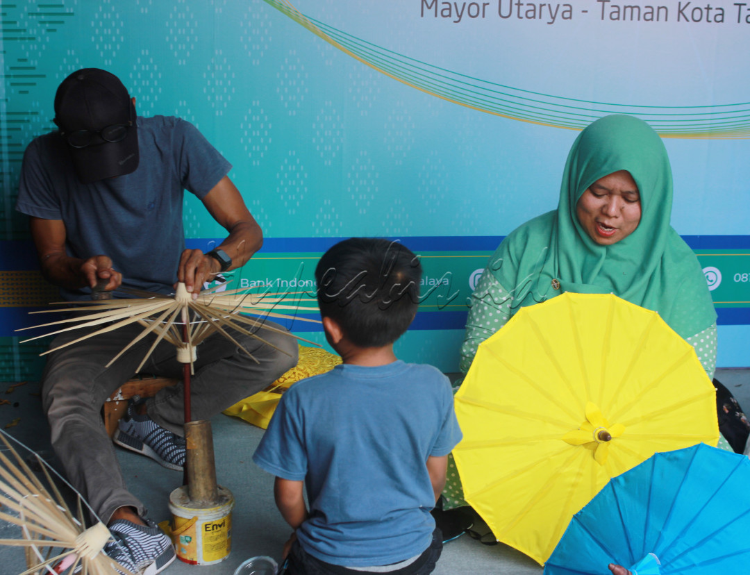 Perajin Payung Geulis foto yang menggambarkan perajin Payung Geulis sedang membuat payung disaksikan anaknya dalam merawat kebhinekaan bidang ekonomi&nbsp;