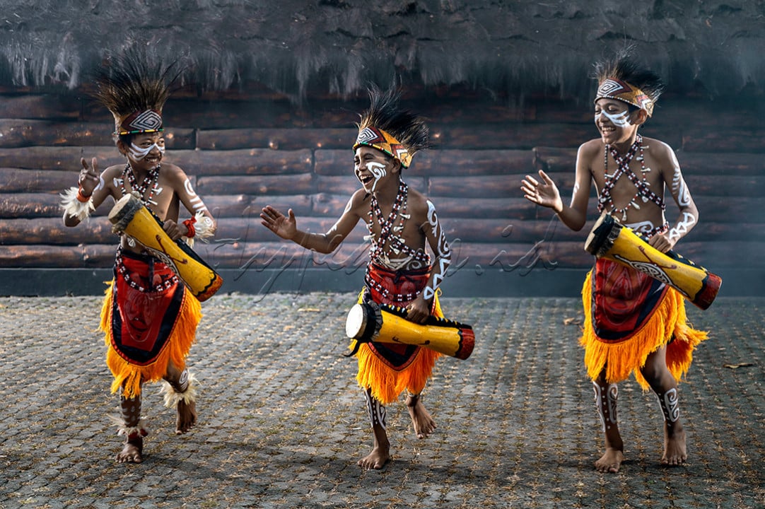 Tiga anak papua sedang menari menghibur pengunjung di Anjungan Papua TMII