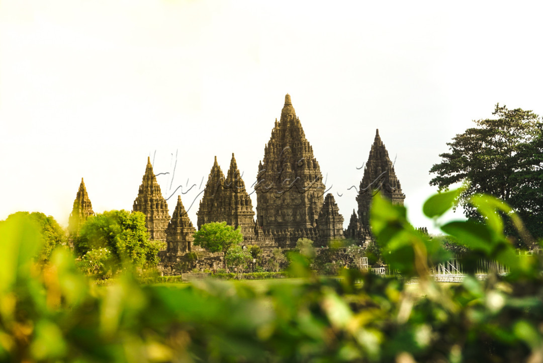 Kemegahan Prambanan: Keajaiban Arsitektur Jawa menampilkan kompleks candi yang menakjubkan di bawah langit cerah dengan nuansa senja yang hangat. Candi Prambanan berdiri megah dengan menara utamanya yang menjulang tinggi, memamerkan detail relief yang rumit dan indah.