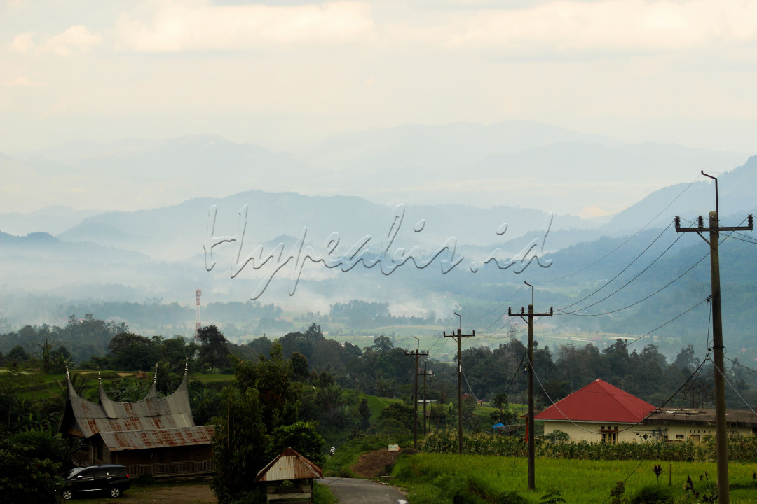 Deretan bukit yang indah diselimuti sebuah awan beserta hijaunya pepohonan dan sebuah sawah tampak memukau pandangan. Foto ini diambil di jalan menuju sebuah desa yang terletak di atas bukit juga sehingga membuat jajaran bukit tampak tersusun menumpuk dengan indah.