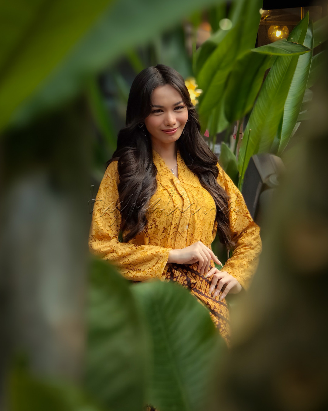 Dalam balutan kebaya kuning, kecantikan dan keanggunan terpancar alami dari wanita ini. Dengan latar dedaunan yang hijau, foto ini menangkap esensi elegan dari warisan budaya Indonesia, memperlihatkan harmoni antara tradisi dan alam.