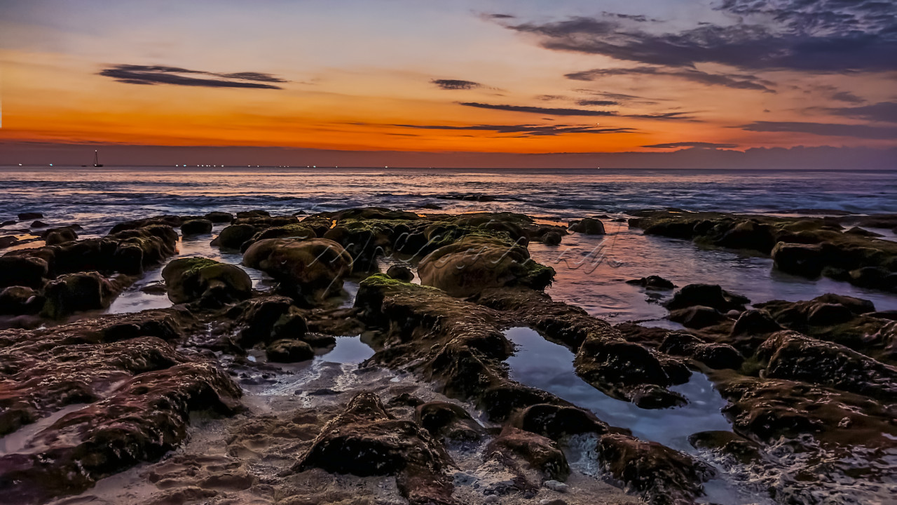 Pantai Indonesia menyuguhkan pemandangan yang memukau saat senja tiba. Warna langit yang bergradasi dari jingga ke ungu berpadu dengan batuan karang yang dihiasi lumut, menciptakan panorama yang seolah melukiskan kedamaian alam. Ombak yang tenang dan garis laut yang membentang luas mengingatkan kita akan kekayaan alam negeri ini, yang tak hanya indah tetapi juga penuh dengan kehidupan. Inilah sekelumit dari pesona Indonesia, di mana keindahan alam dan ketenangan berpadu sempurna.