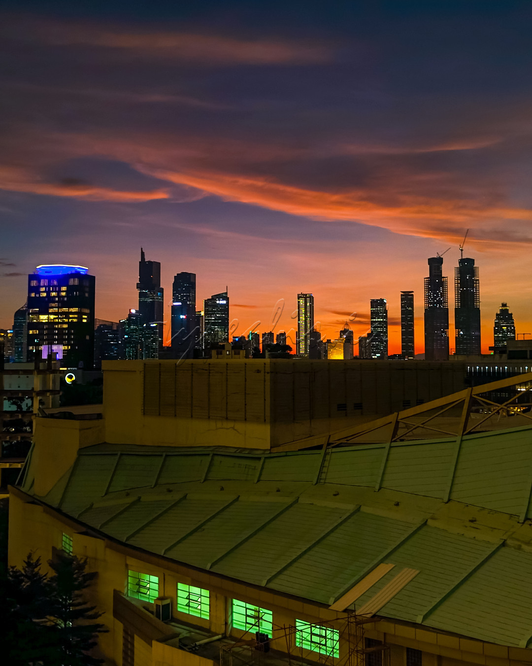 Refleksi visual dari wajah Indonesia yang sedang berubah, di mana kemegahan alam bertemu dengan laju modernisasi. Saat langit senja memancarkan warna-warna hangat, siluet gedung-gedung tinggi berdiri kokoh, menandakan perkembangan pesat di kota-kota besar. Foto ini menggambarkan Indonesia sebagai bangsa yang bergerak maju, dengan kota-kota yang terus berkembang menjadi pusat inovasi dan kemajuan, namun tetap terbingkai dalam keindahan alam yang abadi. Ini adalah potret Indonesia yang memadukan tradisi dan modernitas, memperlihatkan sebuah transformasi.