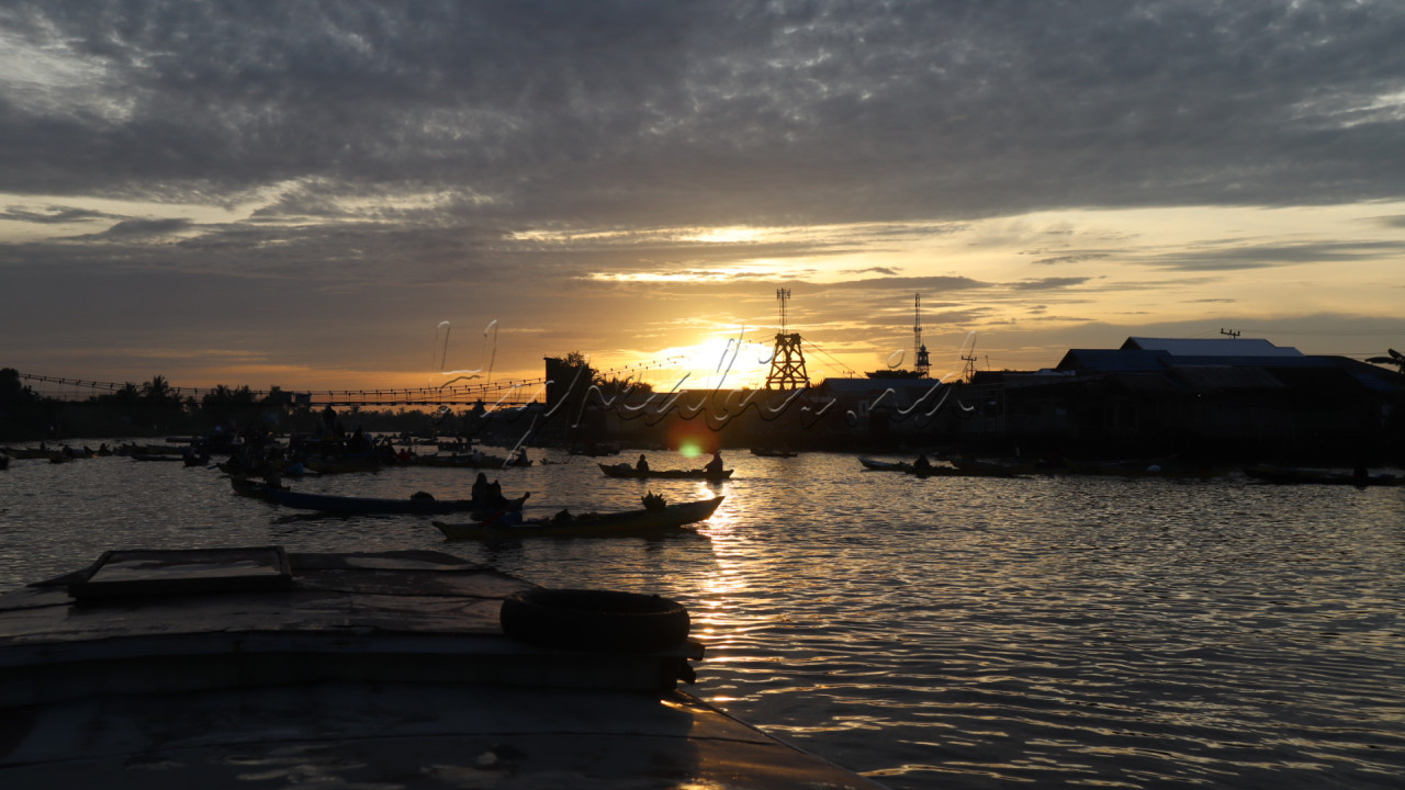 Menggambarkan keindahan matahari terbit yang memantul di air dan siluet perahu pasar terapung lok baintan, Banjarmasin.