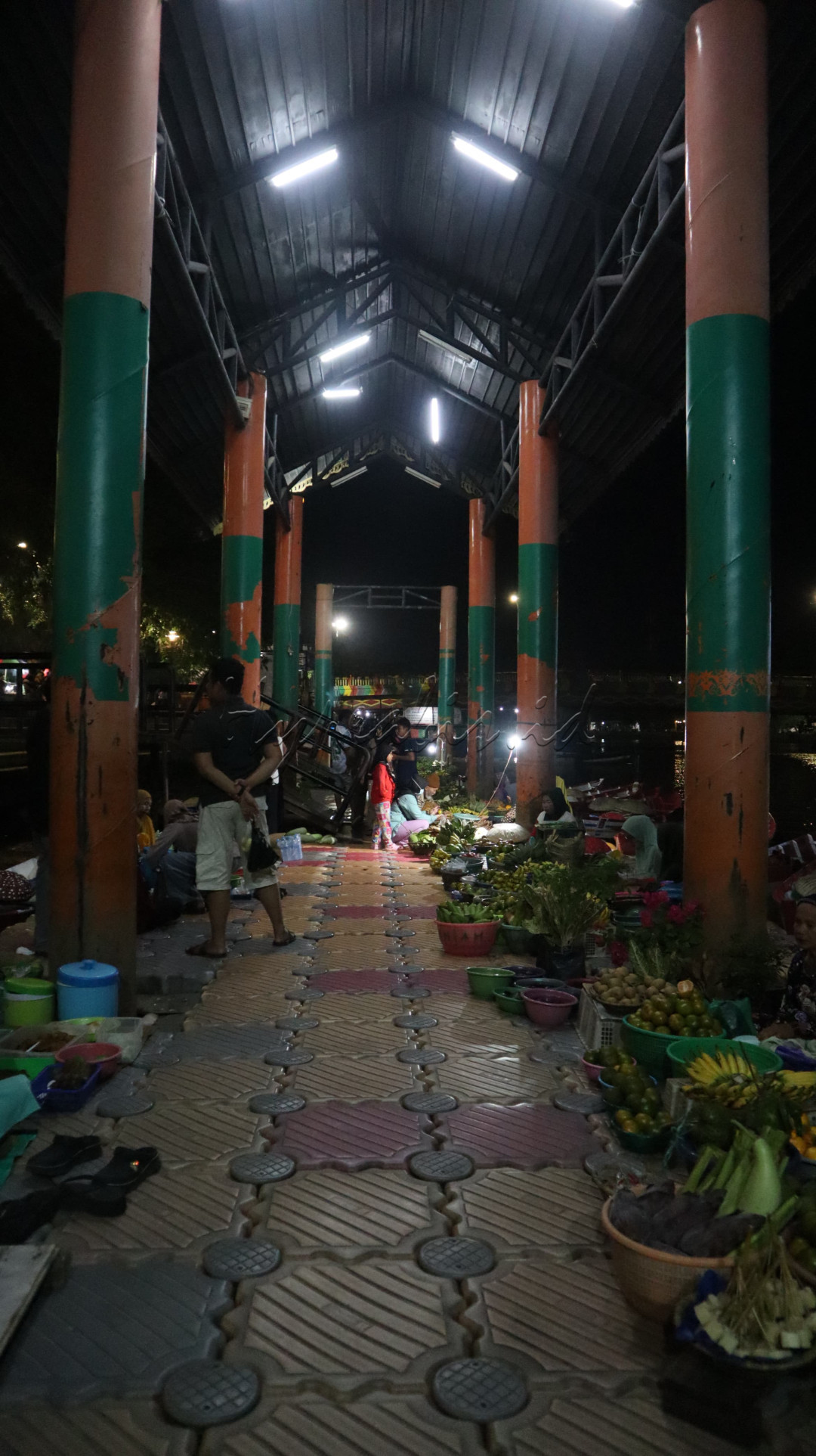 Foto ini membawa kita pada perjalanan singkat ke pasar malam yang penuh dengan keramaian dan warna. Cahaya lampu yang hangat membelai wajah para pedagang dan pengunjung, menciptakan suasana yang nyaman dan penuh keakraban. Setiap sudut pasar menyimpan cerita dan kehidupan yang unik, membuat kita ingin terus menjelajahi setiap lorongnya.