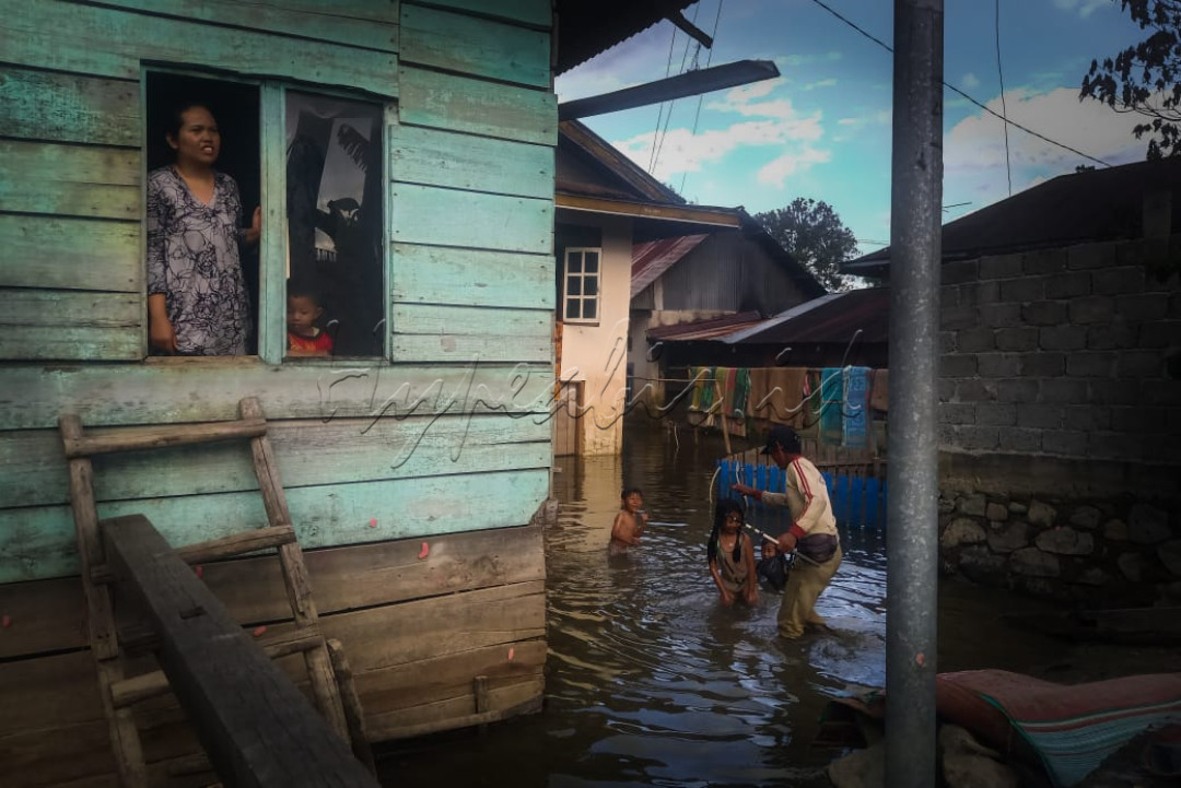 Sebuah potret sebuah keluarga dimana rumah tempat tinggalnya terkena dampak banjir hingga mereka keluar masuk rumah melalui jendela.