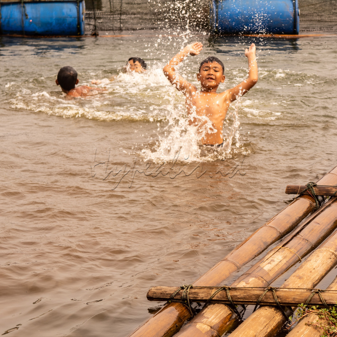 Terdapat anak-anak sedang bermain air di danau, mereka nampak ceria bermain air.