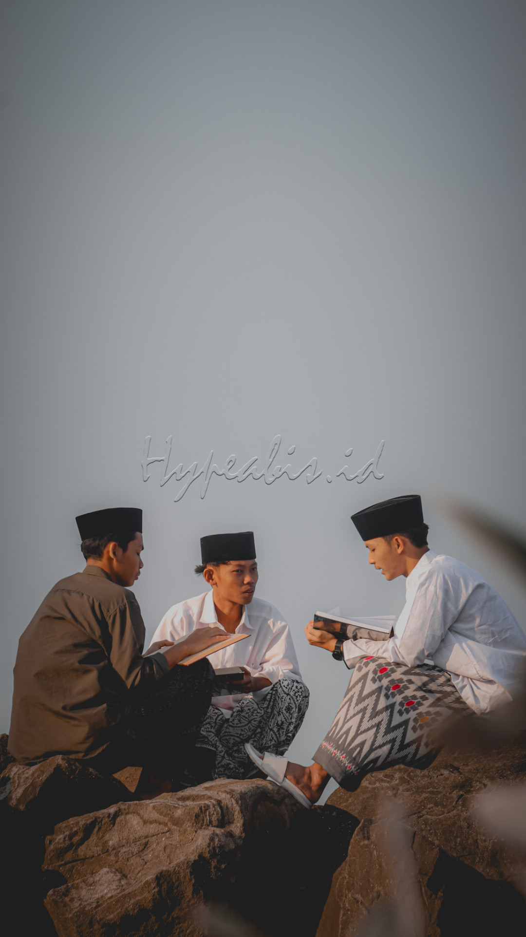 Ketika suasana tenang dan gelombang laut menyatu dengan semangat belajar.&nbsp;tiga santri sedang duduk di bebatuan pesisir pantai, dengan khidmat dan tekun menelaah kitab kitab ulama salaf sambil menikmati aliran segar udara pantai.&nbsp;Foto ini menciptakan gambaran yang menyatukan keindahan alam dan ketenangan belajar dalam suasana yang damai.