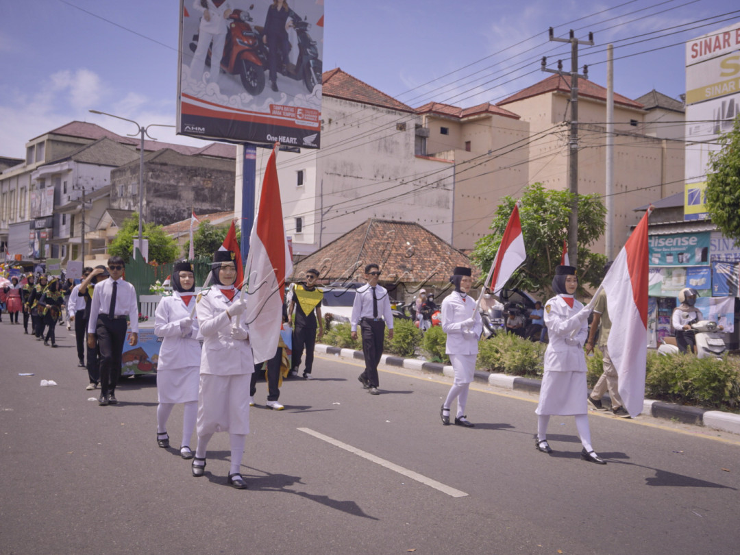 <div>??????Deretan karnaval bertugas pengibar bendera dengan seragam putih berjalan gagah di tengah parade, membawa bendera merah putih dengan penuh rasa bangga. Suasana semarak di tengah kota ini menegaskan semangat nasionalisme dan cinta tanah air yang tetap membara.</div>