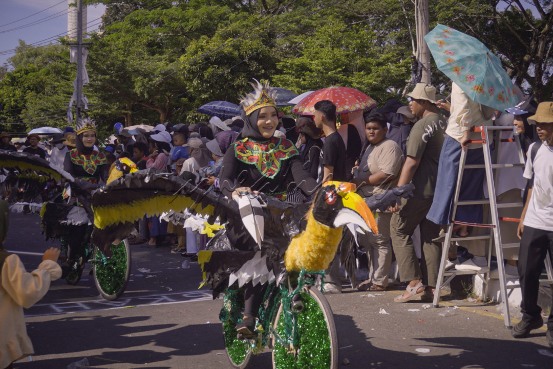 Peserta sepeda hias dengan kostum burung rangkong yang memukau, melintasi kerumunan penonton yang antusias. Dengan hiasan sayap lebar dan warna-warni, mereka menampilkan kekayaan fauna lokal dalam bentuk seni yang kreatif dan menghibur.