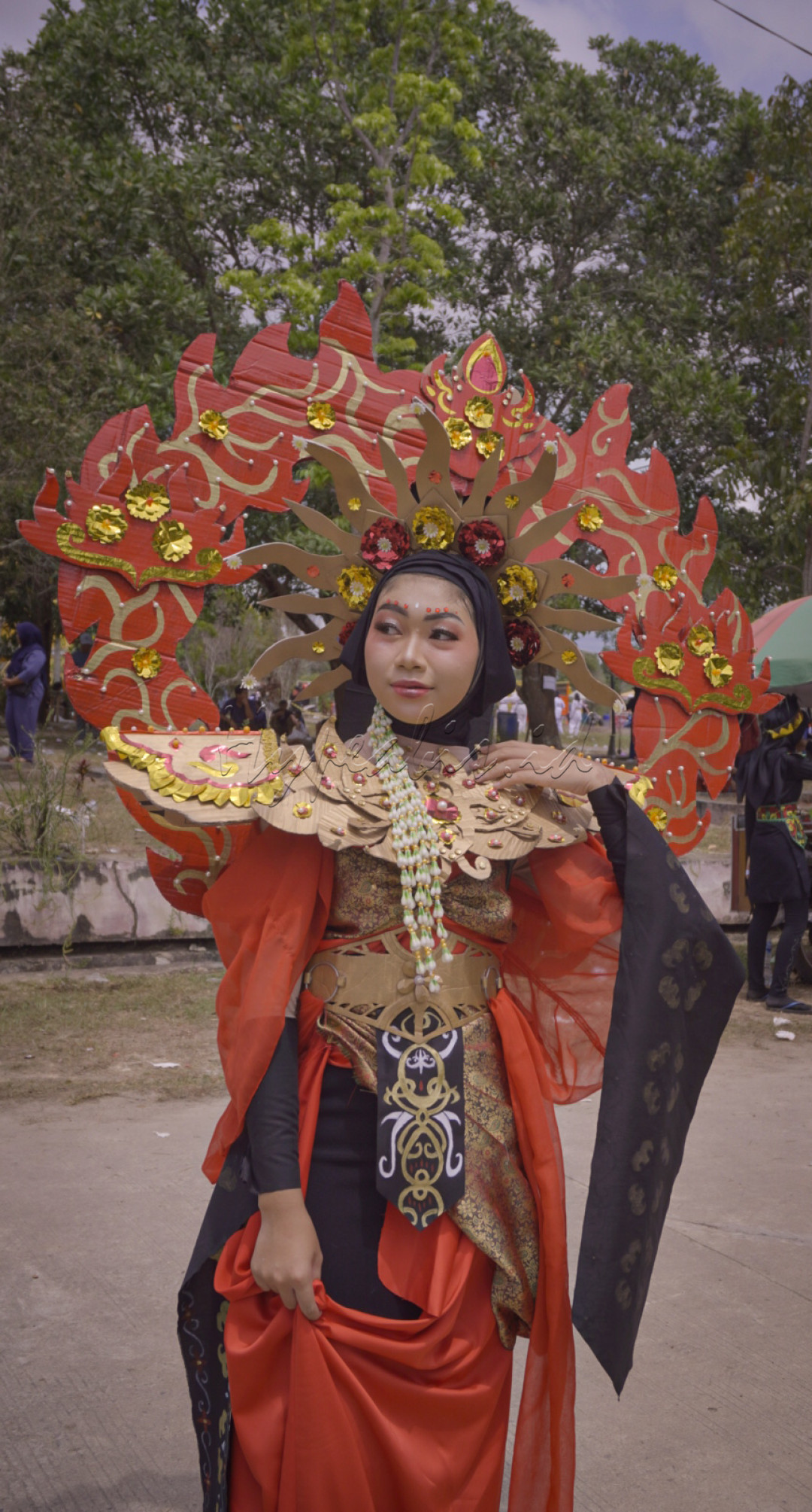 Seorang wanita mengenakan kostum tradisional dengan ornamen megah dan warna merah yang mencolok. Mahkota besar dengan hiasan emas menambah keanggunan dan kemegahan penampilannya, yang mencerminkan kekayaan budaya dalam sebuah perayaan karnaval.