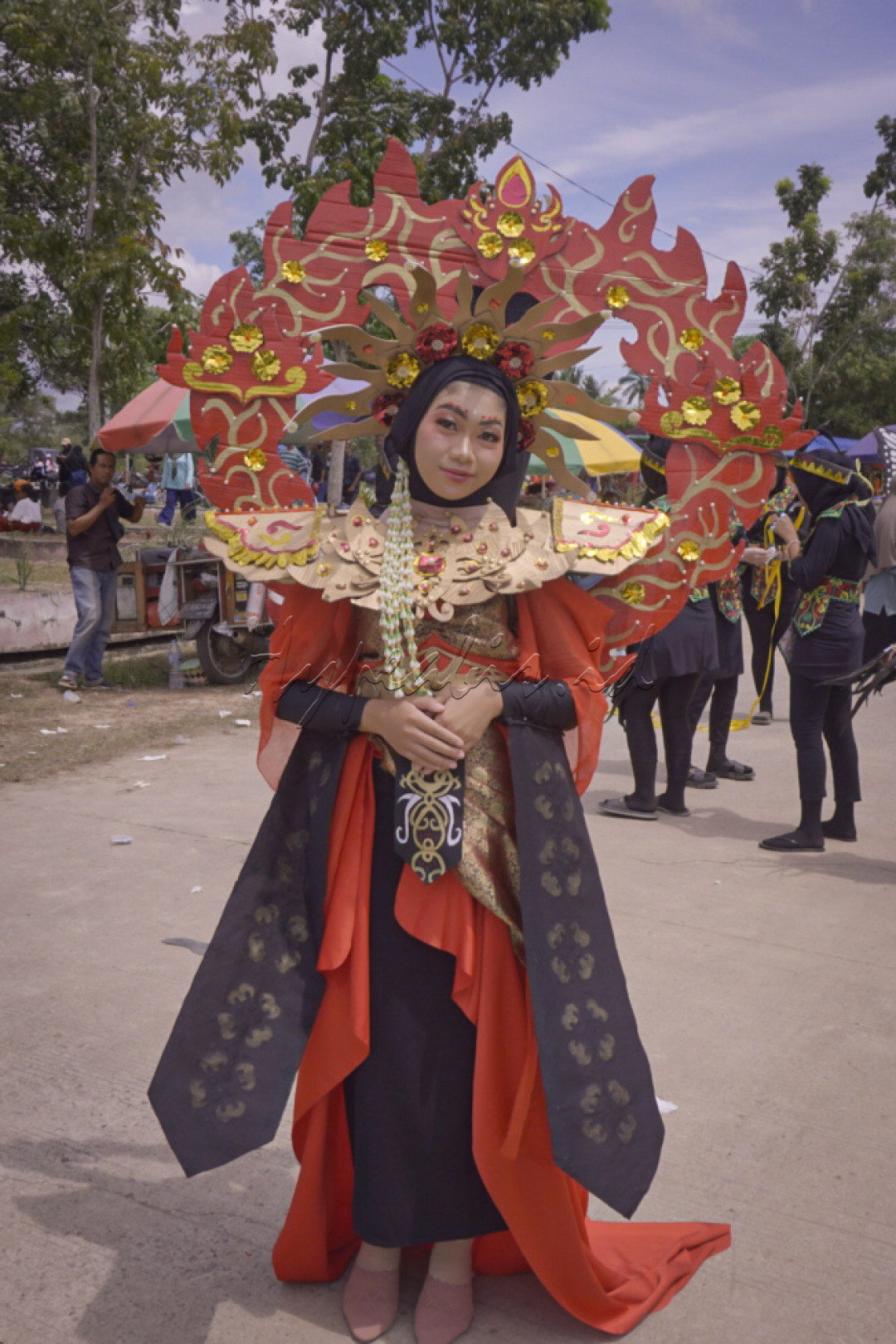 <div>Seorang peserta karnaval tampil anggun dengan kostum tradisional yang memukau. Dengan hiasan kepala yang megah dan busana berwarna merah dan emas, ia mencerminkan kekayaan budaya yang dipadukan dengan kreativitas modern.</div>