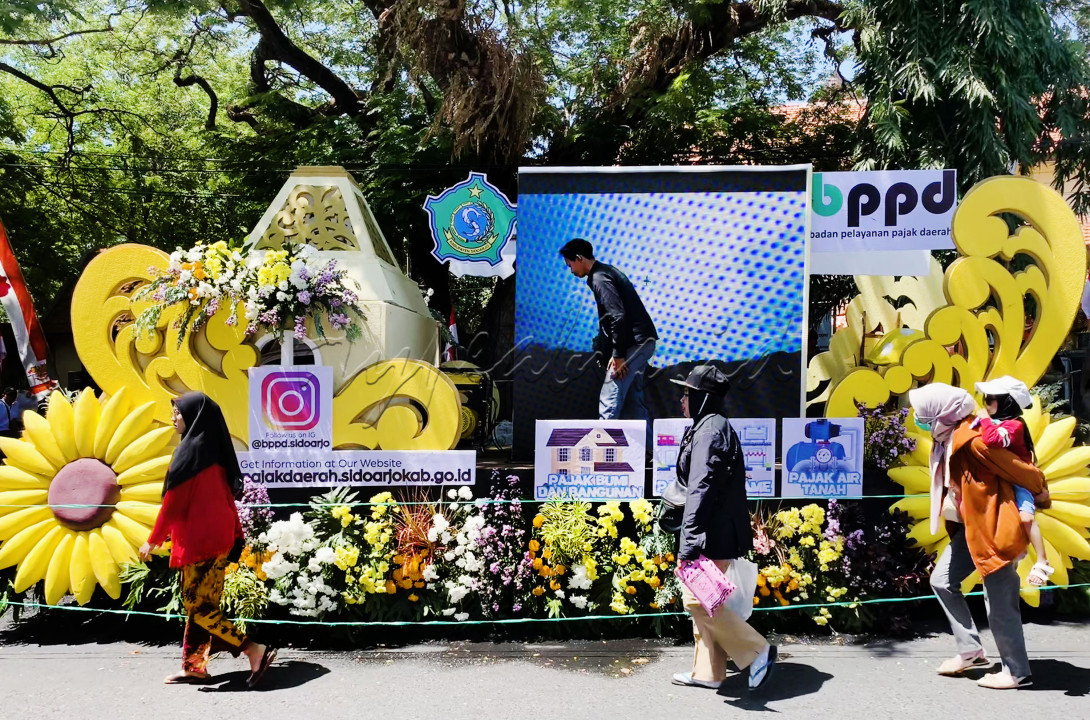 Sebuah mobil pengisi Sidoarjo Carnival 2024 dan hilir mudik orang-orang dalam mempersiapkan diri untuk ikut berpartisipasi dalam acara itu.