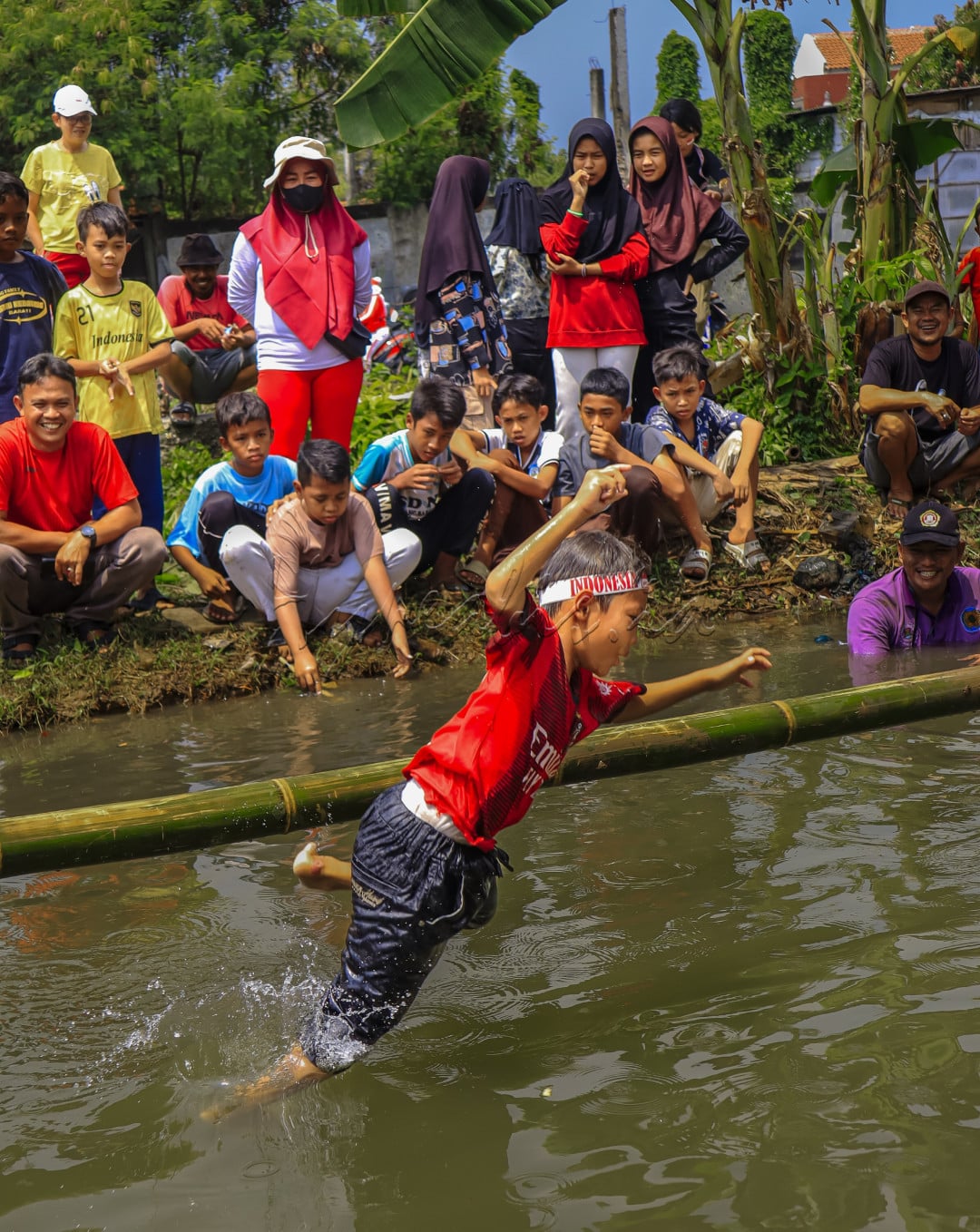 Seorang anak gagal mencapai tujuannya untuk sampai ke ujung bambu, setelah gagal menjaga keseimbangan dan terjatuh ke air.