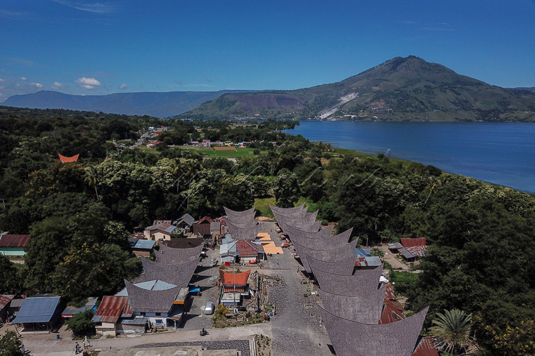 Kawasan Kampung Ulos Huta Raja yang berlokasi di Kecamatan Pangururan, Kabupaten Samosir, Sumatra Utara, Senin (24/6/2024). Kawasan di sekitar Kampung Ulos merupakan wilayah subur dengan banyak tanaman pertanian dan perkebunan. Di area Kampung Ulos terdapat pemukiman di mana, kita dapat melihat warga sekitar yang beraktifitas termasuk dalam pengerjaan kain Ulos. Adapun lokasi koridor pengerjaan ulos yang sekaligus lahan komersial kampung ini merupakan rumah adat Batak yang biasa disebut sebagai Rumah Bolon.&nbsp;