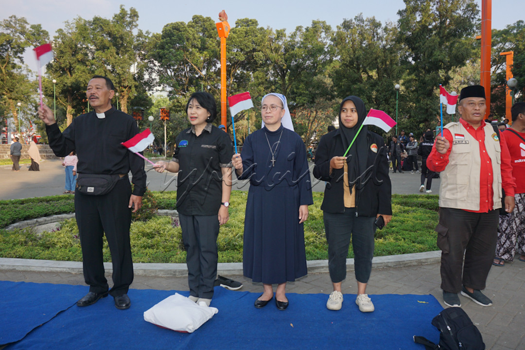 Para pemuka Agama sedang.mengibarkan bendera merah putih saat menyamyikan lagu Hari Merdeka