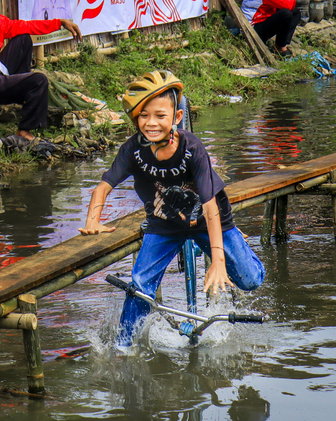 Moment seorsng anak terjatuh setelah sepeda yg dinaikinnya hilang keseimbangan dan tercebur ke air dalam lomba Sepeda lintas papan pada acara 17 Agustusan.