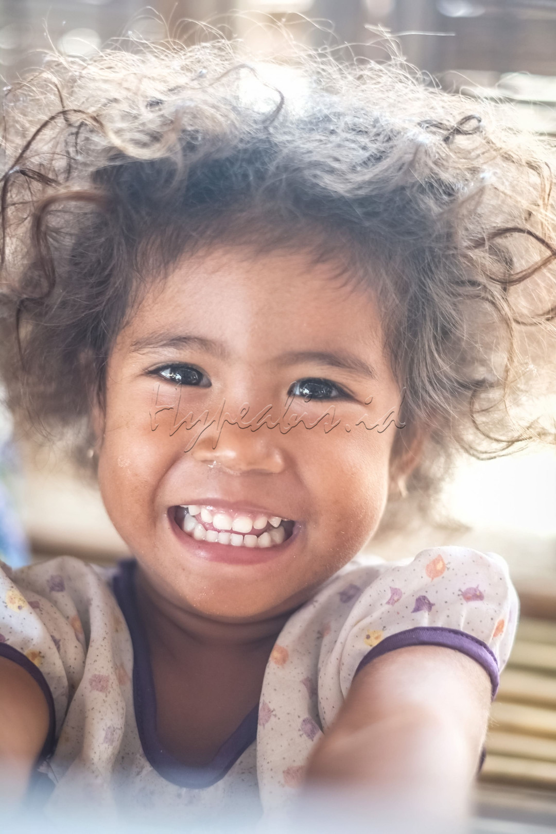 Seorang anak perempuan yang tersenyum lebar dan terlihat bahagia.