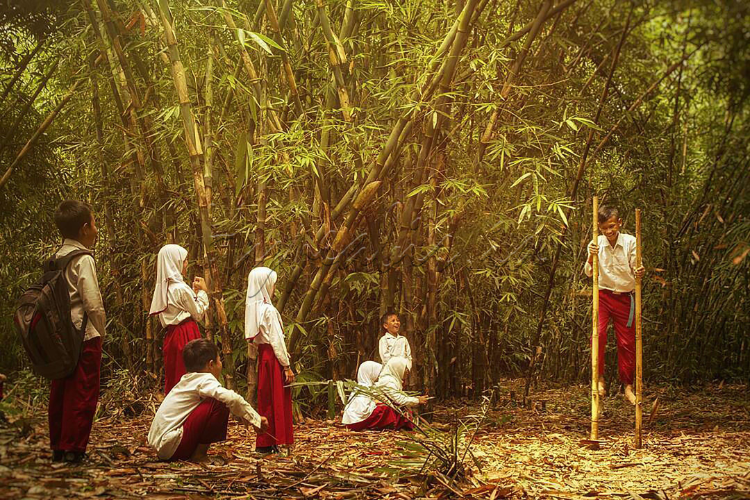 Anak - anak Sekolah Dasar yang sedang beristirahat dan bermain engrang di tengah hutan bambu bersama cahaya hangat matahari.