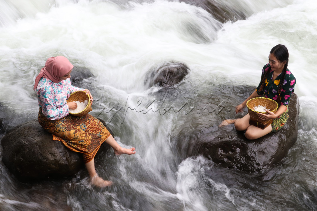 Dua gadis desa sedang bercengkerama di sungai sambil mencuci beras.