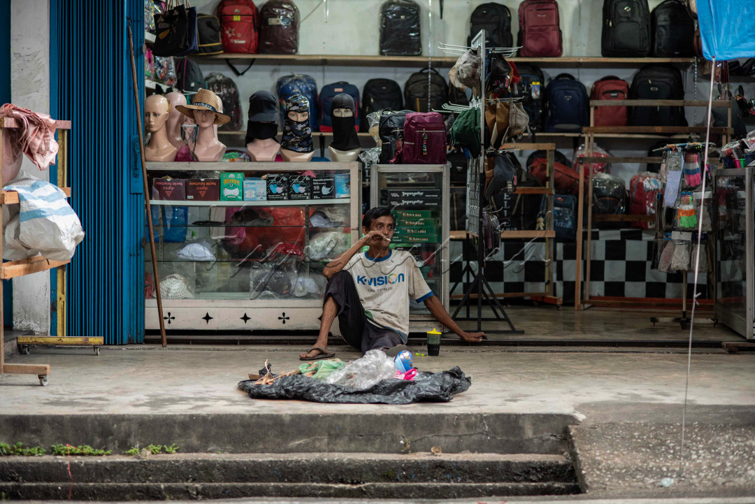 Bapak pekerja lepas mengistirahkan diri dan merenung dengan sebatang rokok dan segelas kopi didepan toko busana.