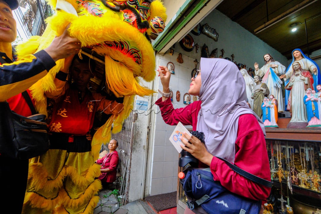 Seorang Muslimah turut memberi angpao kepada pemain barongsai di depan sebuah toko rohani Kristiani.