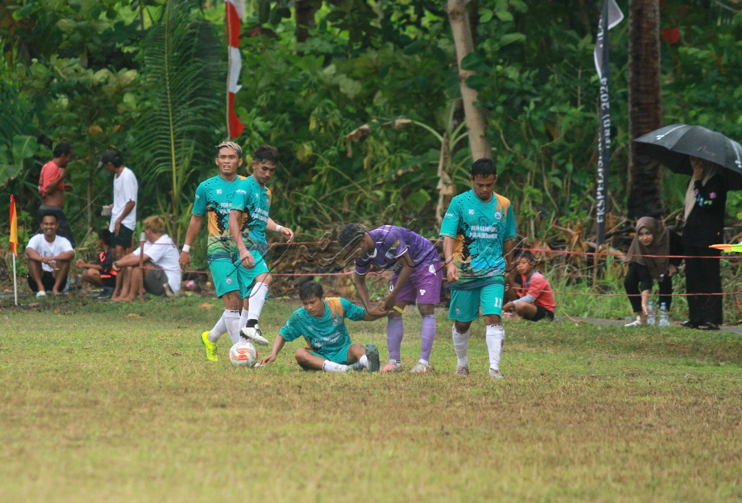 Seorang pemain berusaha membantu lawannya yang terjatuh sebagai bentuk sportivitas dalam olahraga sepakbola