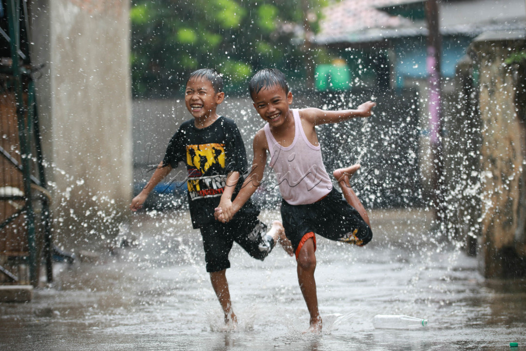 Dua anak laki-laki bermain dengan riang di tengah hujan deras. Anak yang berada di sebelah kanan tampak berlari dengan penuh semangat sambil mengacungkan tangan kanannya ke arah kamera. Ekspresi wajahnya menggambarkan kegembiraan yang meluap. Di sampingnya, seorang anak laki-laki lainnya ikut berlari dengan senyum lebar yang terukir di wajahnya. Keduanya tampak menikmati setiap tetes air hujan yang membasahi tubuh mereka.<br />
<br />
&nbsp;Hujan lebat yang turun tidak menyurutkan semangat dua anak laki-laki ini untuk bermain. Mereka memanfaatkan waktu luang mereka untuk bersenang-senang di tengah derasnya hujan. Meskipun pakaian mereka basah kuyup, mereka tetap tertawa dan bermain dengan riang. Raut wajah mereka yang penuh kebahagiaan menunjukkan bahwa bermain di tengah hujan adalah hal yang menyenangkan bagi mereka.<br />
<br />
Gambar ini menggambarkan betapa sederhana dan menyenangkannya hidup di masa kanak-kanak. Hal-hal kecil seperti bermain di tengah hujan dapat memberikan kebahagiaan dan kenangan yang tak terlupakan. Gambar ini juga mengingatkan kita tentang pentingnya menghargai momen-momen sederhana dalam hidup, karena hal itulah yang sering kali membuat hidup kita lebih bermakna.<br />
<br />
<br />
<br />
&nbsp;