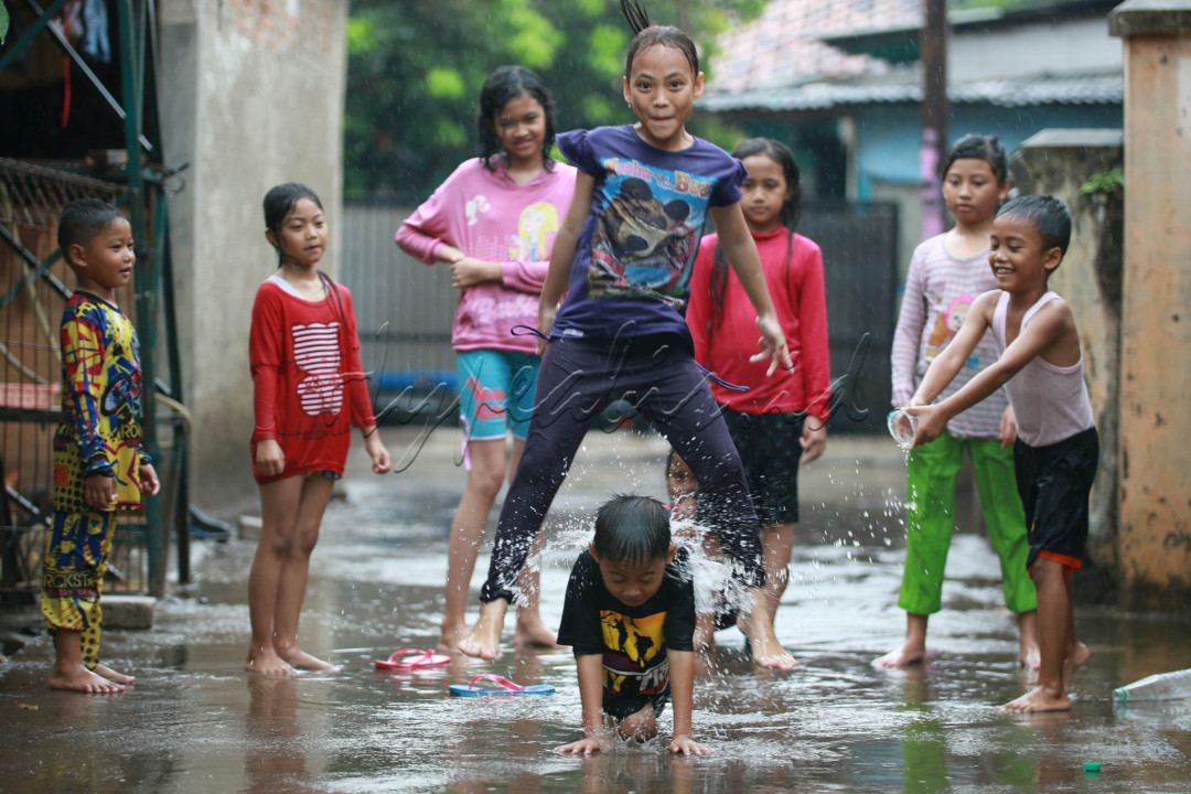 Foto ini menunjukkan sekelompok anak-anak yang sedang bermain di tengah hujan. Terlihat anak-anak tersebut sangat menikmati suasana hujan dengan berlarian dan saling menyiram air. Ekspresi wajah mereka yang gembira menunjukkan betapa menyenangkannya bermain di hujan.<br />
<br />
Beberapa anak mengenakan pakaian berwarna cerah, seperti merah, kuning, dan hijau. Hal ini menambah keceriaan dan warna pada gambar. Di antara mereka, ada seorang anak perempuan yang sedang melompat dengan penuh semangat sambil tersenyum.<br />
<br />
Foto ini menggambarkan keceriaan dan kegembiraan anak-anak dalam menikmati alam. Mereka tidak peduli dengan hujan yang membasahi tubuh mereka, yang penting mereka bisa bermain bersama-sama.