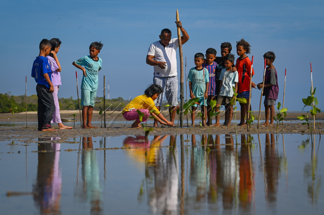 Nelayan yag juga aktivis lingkungan Muhammad Mansur Dokeng (tengah) mengajari anak-anak tentang pentingnya tanaman bakau (mangrove) bagi lingkungan pesisir di Pantai Oesapa, Kupang, Nusa Tenggara Timur, Jumat (28/6/2024).